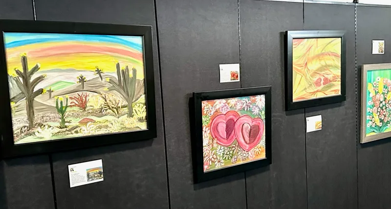 Framed desert cactus, heart, and floral paintings on a black gallery wall.